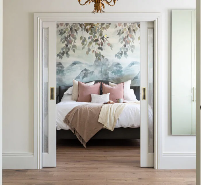 View of principal bedroom through sliding pocket doors, pink and blue tones with scenic wallpaper