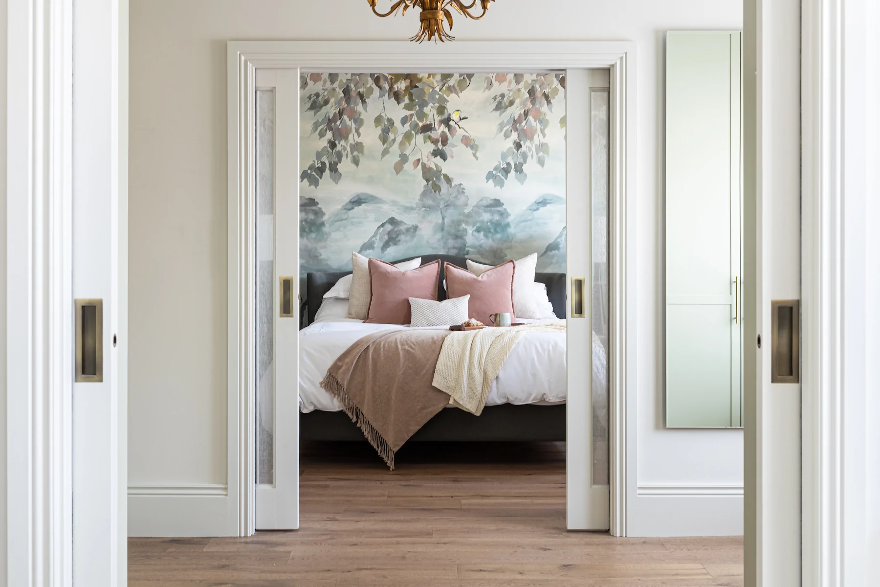 View of principal bedroom through sliding pocket doors, pink and blue tones with scenic wallpaper