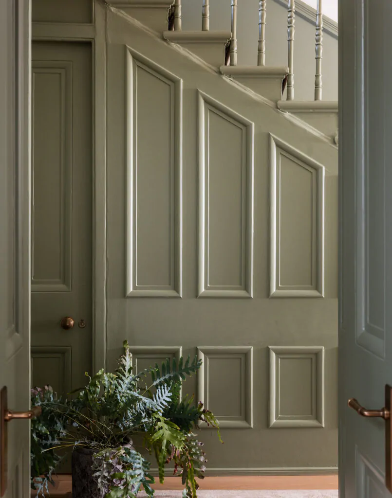 Traditional panelled staircase in green paint with large plant