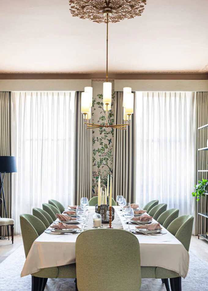 Grand Regenecy townhouse dining room with pink ceiling and cornice, bold patterned tree wallpaper and a set dining table with green chairs, candles, crockery