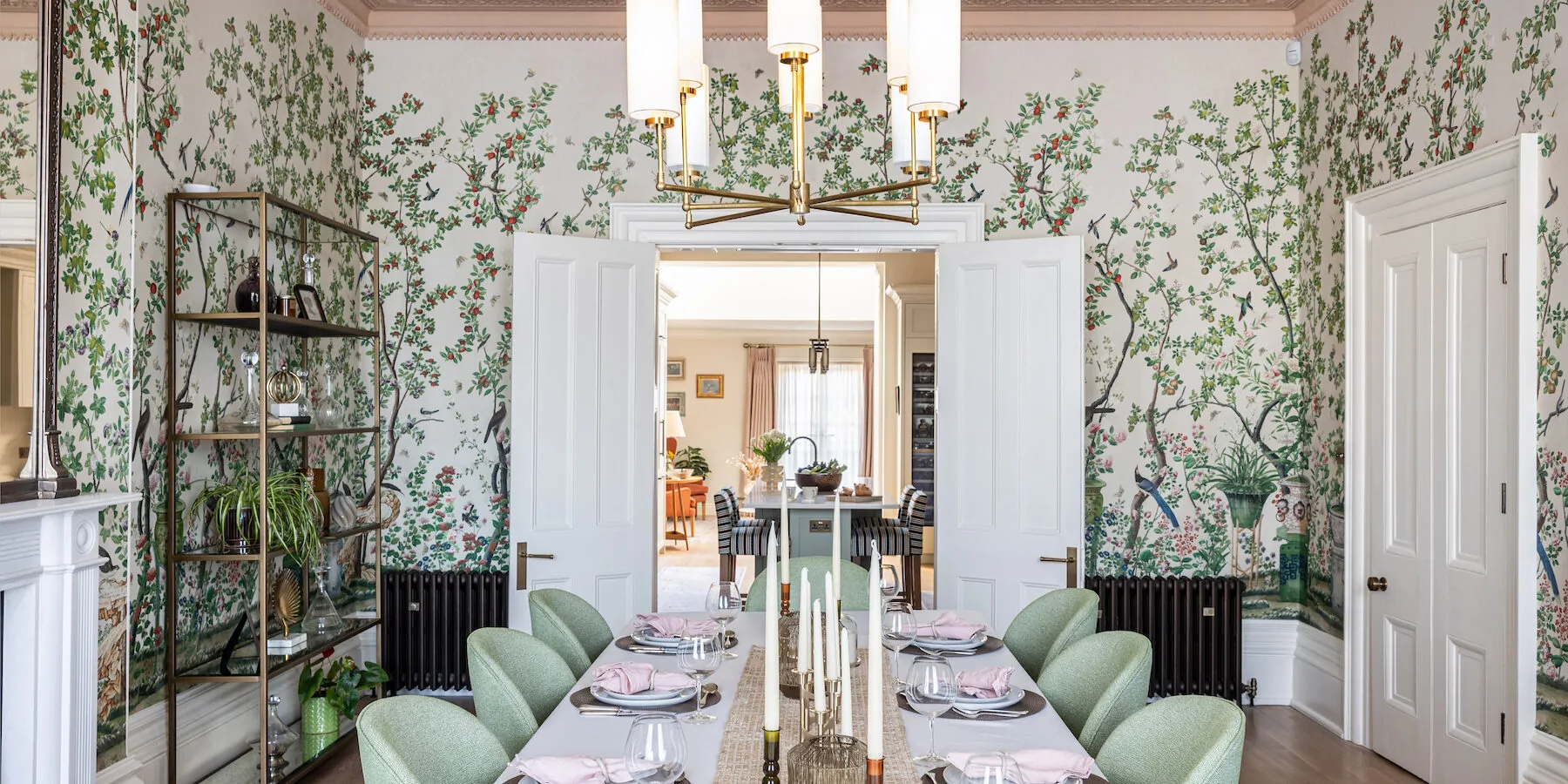 Grand Regenecy townhouse dining room with pink ceiling and cornice, bold patterned tree wallpaper and a set dining table with green chairs, candles, crockery